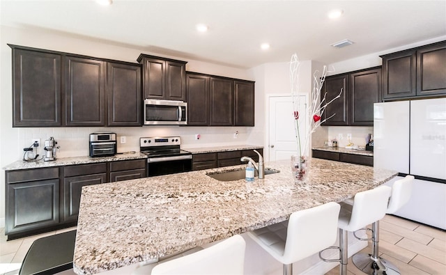 kitchen with light stone countertops, sink, stainless steel appliances, a kitchen breakfast bar, and a kitchen island with sink