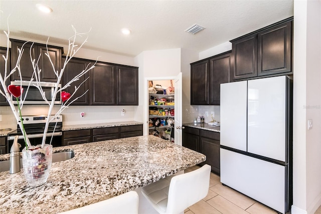 kitchen featuring sink, decorative backsplash, light stone countertops, appliances with stainless steel finishes, and dark brown cabinets