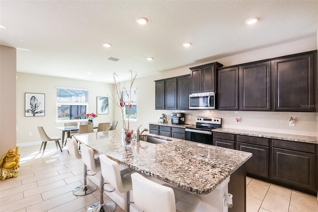 kitchen featuring dark brown cabinetry, sink, a breakfast bar area, a center island with sink, and appliances with stainless steel finishes