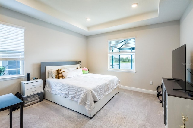 bedroom with light carpet, a raised ceiling, and multiple windows