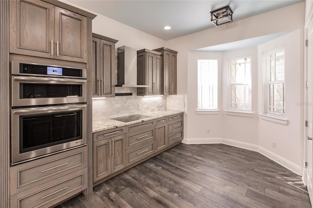 kitchen featuring light stone countertops, wall chimney exhaust hood, black electric cooktop, double oven, and dark hardwood / wood-style floors