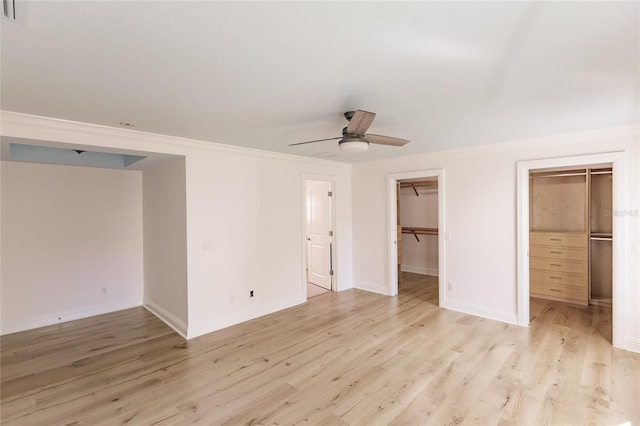 unfurnished bedroom featuring ceiling fan, a walk in closet, crown molding, and light hardwood / wood-style flooring