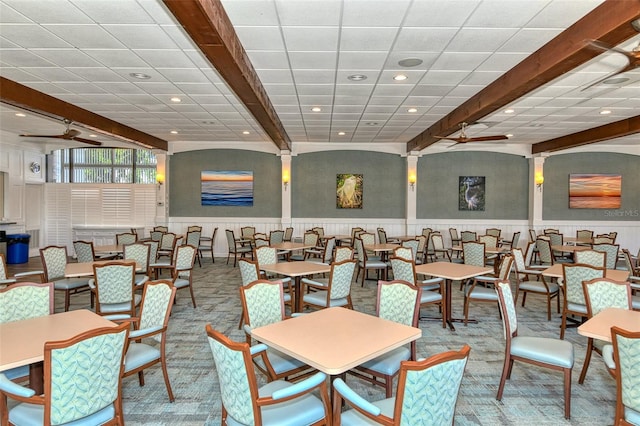 dining area with ceiling fan, beamed ceiling, and light colored carpet