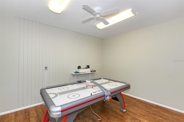 rec room featuring wooden walls, ceiling fan, and dark wood-type flooring