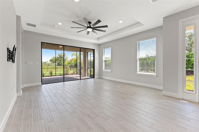 unfurnished room with ceiling fan, a tray ceiling, and light hardwood / wood-style flooring