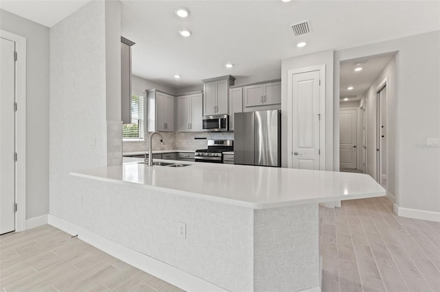 kitchen with sink, appliances with stainless steel finishes, gray cabinetry, a kitchen breakfast bar, and kitchen peninsula