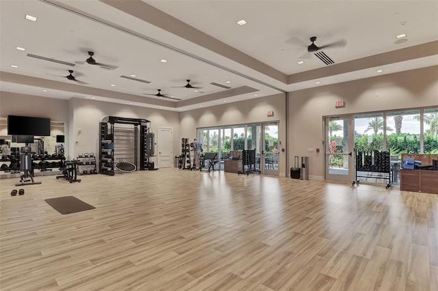 workout area featuring a high ceiling, light hardwood / wood-style floors, and a tray ceiling