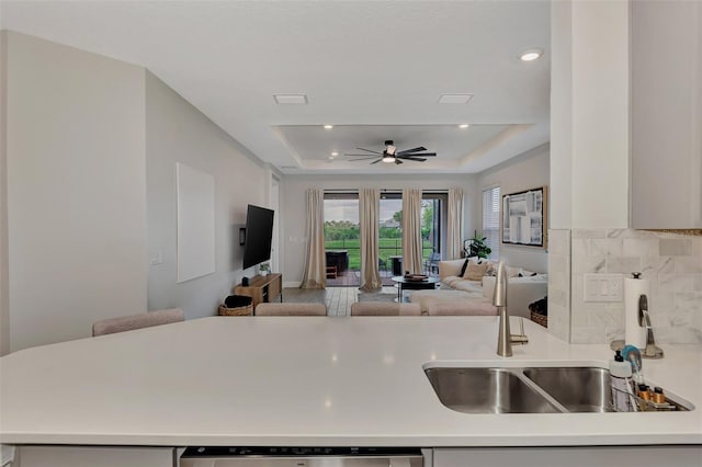 kitchen featuring sink, tasteful backsplash, stainless steel dishwasher, a tray ceiling, and ceiling fan