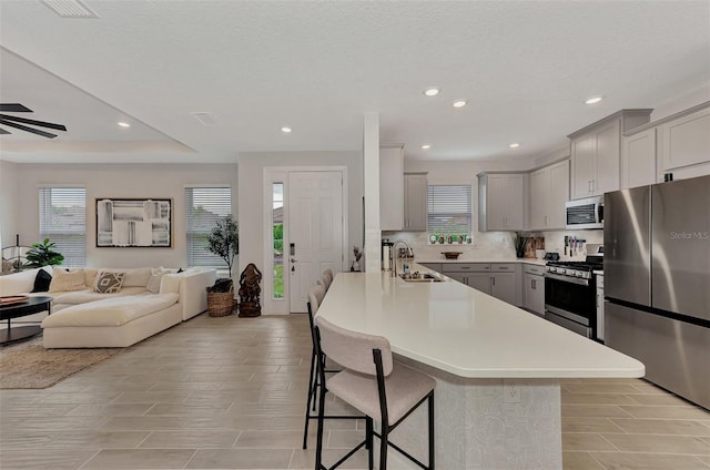 kitchen with sink, gray cabinets, a breakfast bar area, stainless steel appliances, and a healthy amount of sunlight