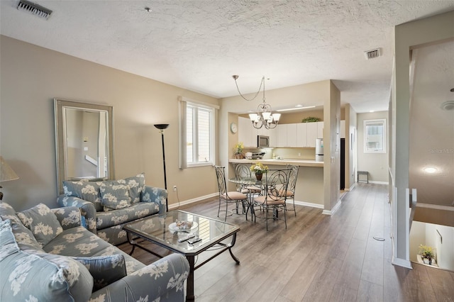 living room featuring a textured ceiling, light wood-type flooring, and a notable chandelier