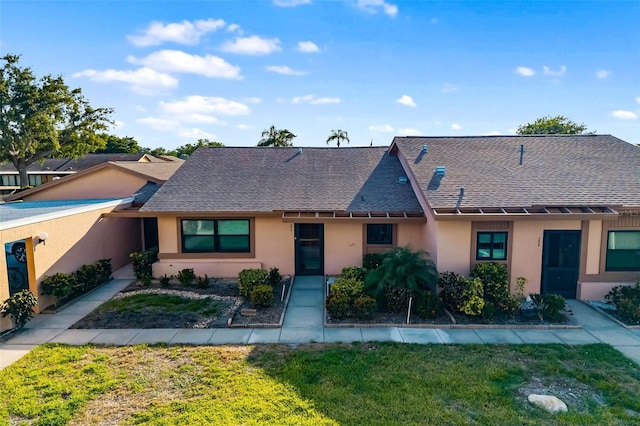 view of property featuring a shingled roof, stucco siding, and a front yard