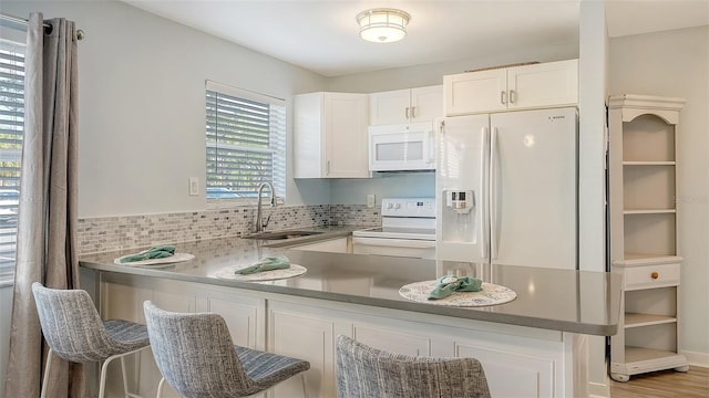 kitchen featuring white cabinetry, sink, backsplash, kitchen peninsula, and white appliances