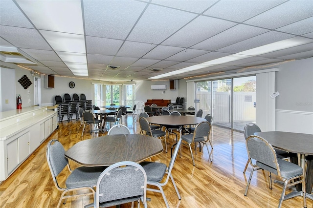 dining room with light wood-type flooring, an AC wall unit, and a paneled ceiling