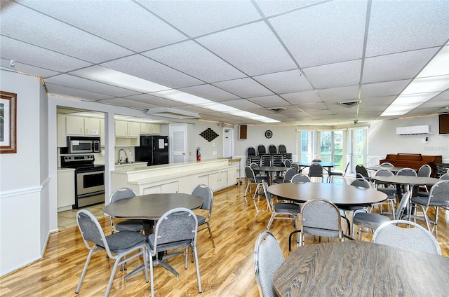 dining space with light wood-type flooring, a drop ceiling, a wall mounted AC, and sink