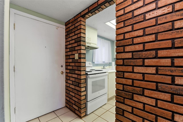 kitchen featuring electric stove, a textured ceiling, light tile patterned floors, white cabinets, and brick wall