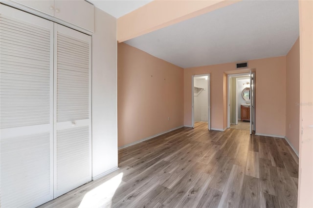 unfurnished bedroom with wood-type flooring, ensuite bath, and a closet