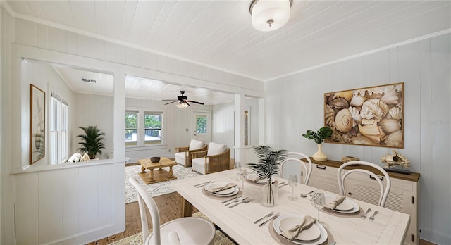 dining area with hardwood / wood-style floors, wooden walls, ceiling fan, and ornamental molding