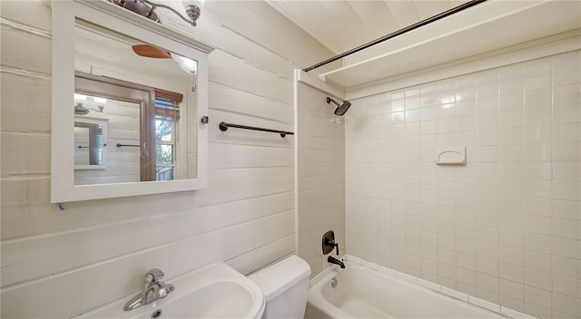 full bathroom with wood walls, sink, tiled shower / bath combo, and toilet