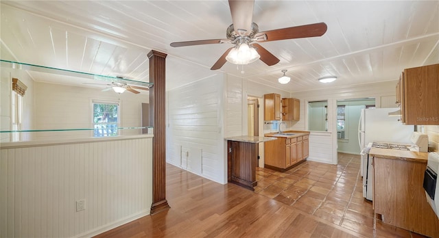 kitchen with ceiling fan, sink, stove, wooden walls, and light wood-type flooring