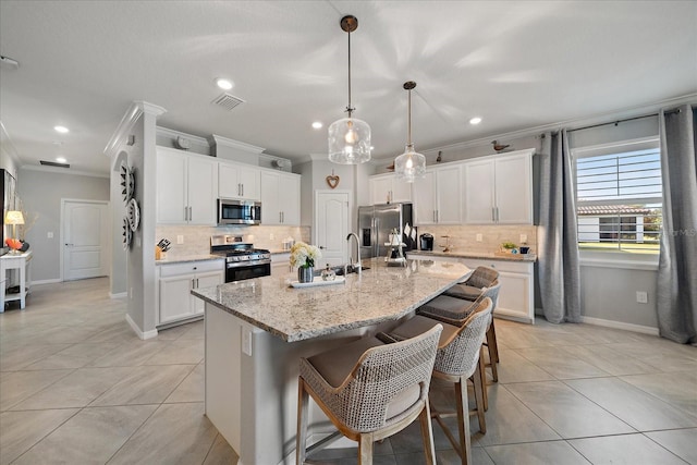 kitchen featuring stainless steel appliances, decorative light fixtures, a center island with sink, white cabinets, and ornamental molding