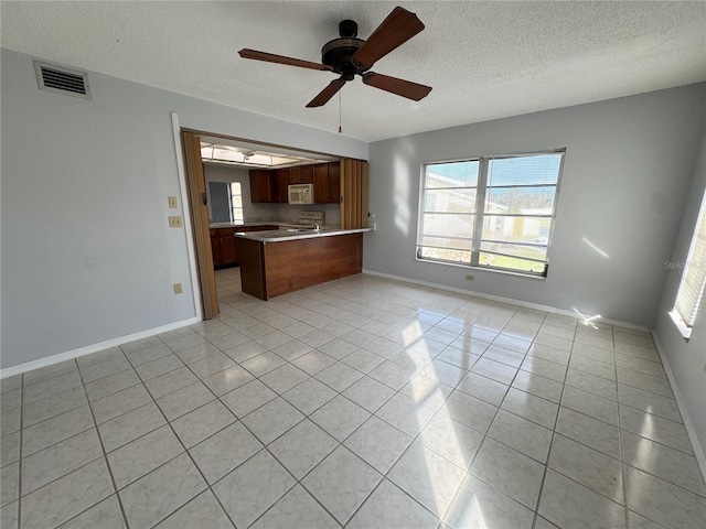 kitchen with kitchen peninsula, ceiling fan, light tile patterned flooring, and a textured ceiling