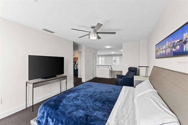 bedroom featuring ceiling fan, a closet, dark carpet, and a spacious closet