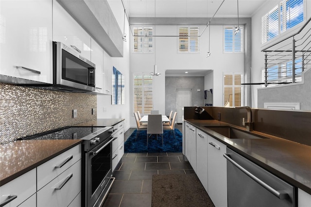 kitchen with stainless steel appliances, dark tile patterned floors, sink, white cabinetry, and hanging light fixtures