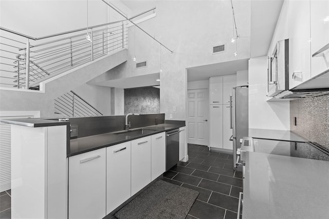 kitchen with sink, a high ceiling, kitchen peninsula, white cabinets, and appliances with stainless steel finishes