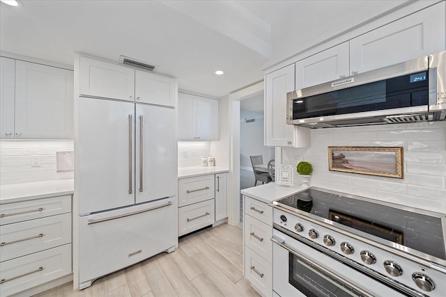 kitchen with decorative backsplash, high quality appliances, light hardwood / wood-style flooring, and white cabinets