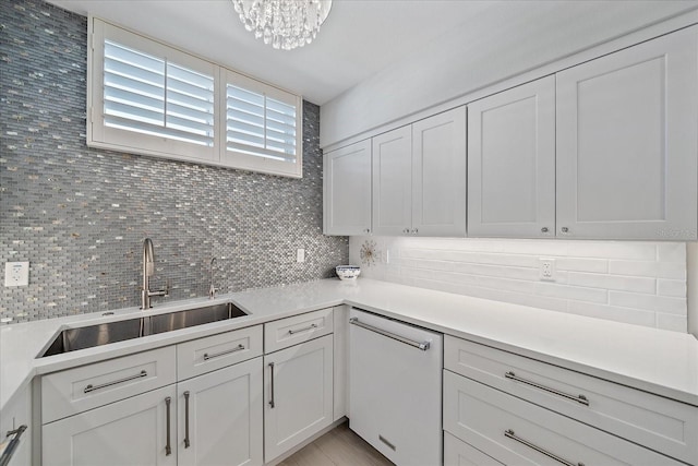 kitchen featuring decorative backsplash, sink, an inviting chandelier, dishwasher, and white cabinetry