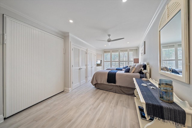 bedroom featuring ceiling fan, light hardwood / wood-style floors, two closets, and ornamental molding