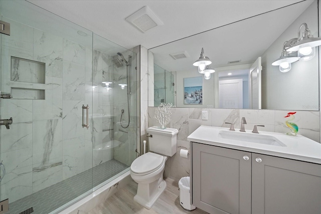 bathroom with hardwood / wood-style floors, toilet, vanity, a shower with shower door, and tile walls