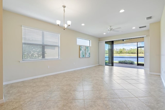 tiled spare room with ceiling fan with notable chandelier and a wealth of natural light