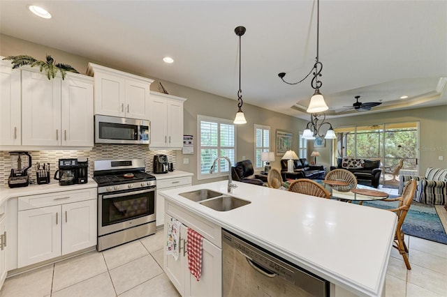 kitchen with sink, stainless steel appliances, an island with sink, white cabinets, and ceiling fan with notable chandelier