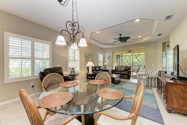 tiled dining room featuring ceiling fan with notable chandelier, a tray ceiling, and a wealth of natural light