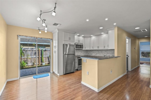 kitchen with kitchen peninsula, appliances with stainless steel finishes, tasteful backsplash, white cabinets, and light hardwood / wood-style floors