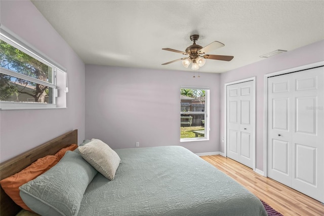 bedroom with wood-type flooring, two closets, and ceiling fan