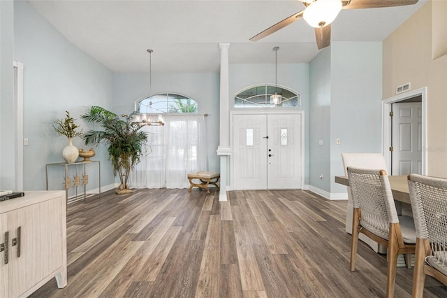 entryway featuring ornate columns, ceiling fan with notable chandelier, dark wood-type flooring, and a high ceiling