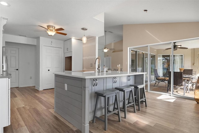 kitchen featuring a large island with sink, vaulted ceiling, light hardwood / wood-style floors, and white cabinetry