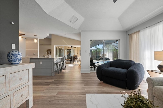 living room with a textured ceiling, light wood-type flooring, and lofted ceiling