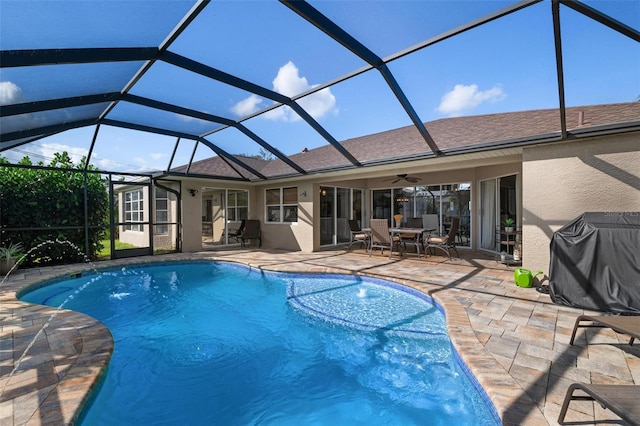 view of pool featuring glass enclosure, pool water feature, ceiling fan, a grill, and a patio area