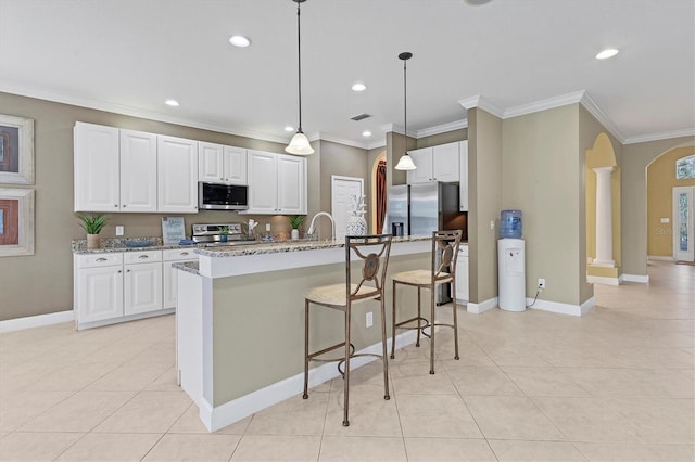 kitchen featuring white cabinets, ornamental molding, an island with sink, light stone counters, and stainless steel appliances