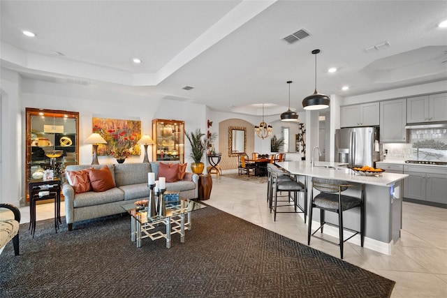 living room featuring light tile patterned flooring, a raised ceiling, and sink