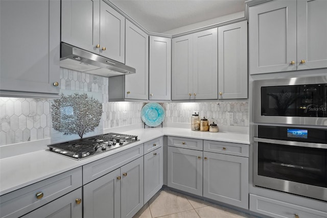 kitchen featuring gray cabinetry, light tile patterned floors, backsplash, and appliances with stainless steel finishes