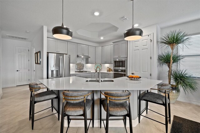 kitchen with sink, stainless steel appliances, tasteful backsplash, pendant lighting, and a center island with sink