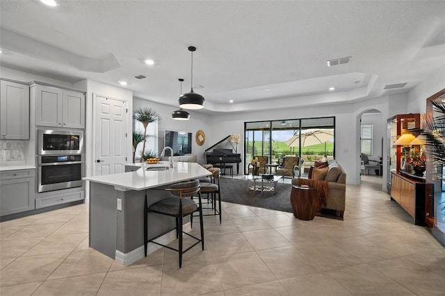 kitchen with pendant lighting, gray cabinetry, a center island with sink, sink, and a kitchen bar