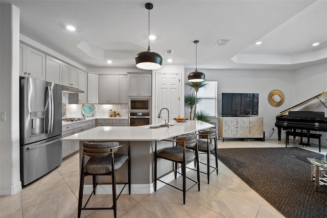 kitchen featuring a tray ceiling, a center island with sink, decorative light fixtures, and appliances with stainless steel finishes