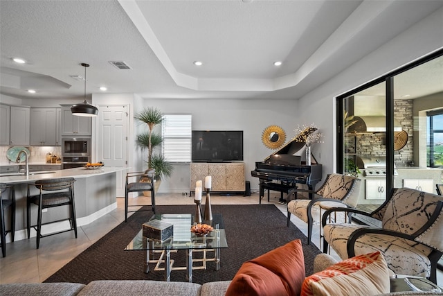 living room featuring a raised ceiling, a healthy amount of sunlight, light tile patterned flooring, and sink