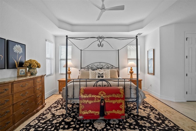 tiled bedroom featuring ceiling fan and a tray ceiling