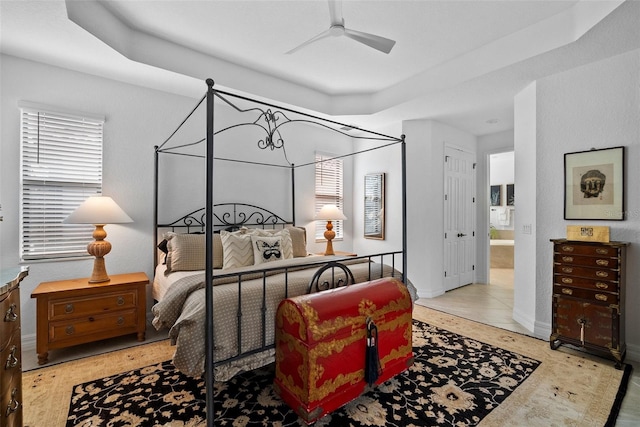 bedroom with ceiling fan, a tray ceiling, and ensuite bath